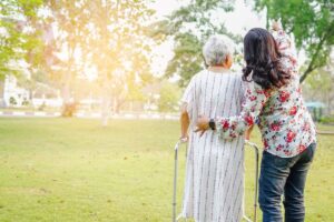 A professional caregiver sitting with an older adult at a kitchen table reviewing paperwork together.