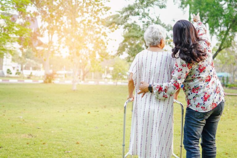 A professional caregiver sitting with an older adult at a kitchen table reviewing paperwork together.