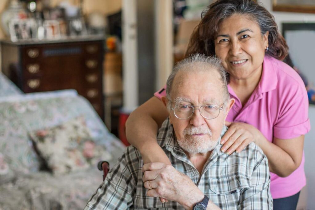 An older adult using a walker walks safely through a well-lit, tidy living room with clear walkways.