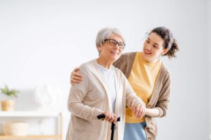 An elderly person and a middle-aged adult sit on a porch, talking gently as they hold hands.