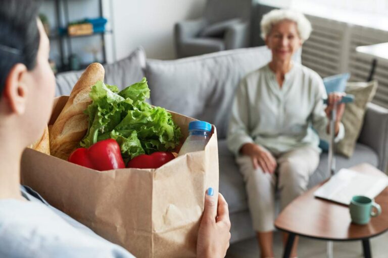 Older adult reviewing a medication chart beside labeled pill containers at a kitchen table.
